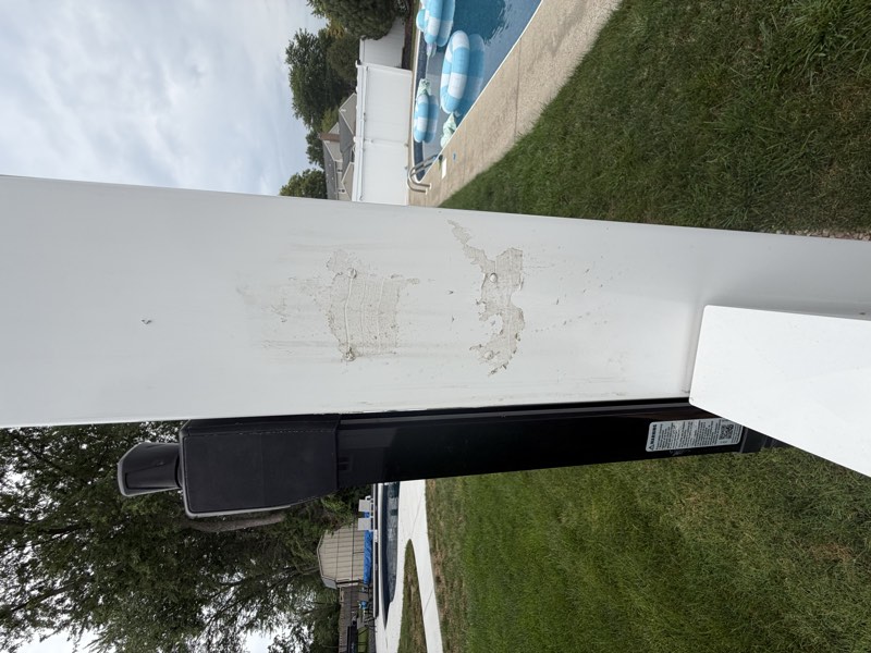 Caulk patches on a pool gate post beside black gate closer hardware, with the swimming pool behind.